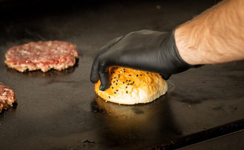 Chef putting burger bun and meat patty on griddle