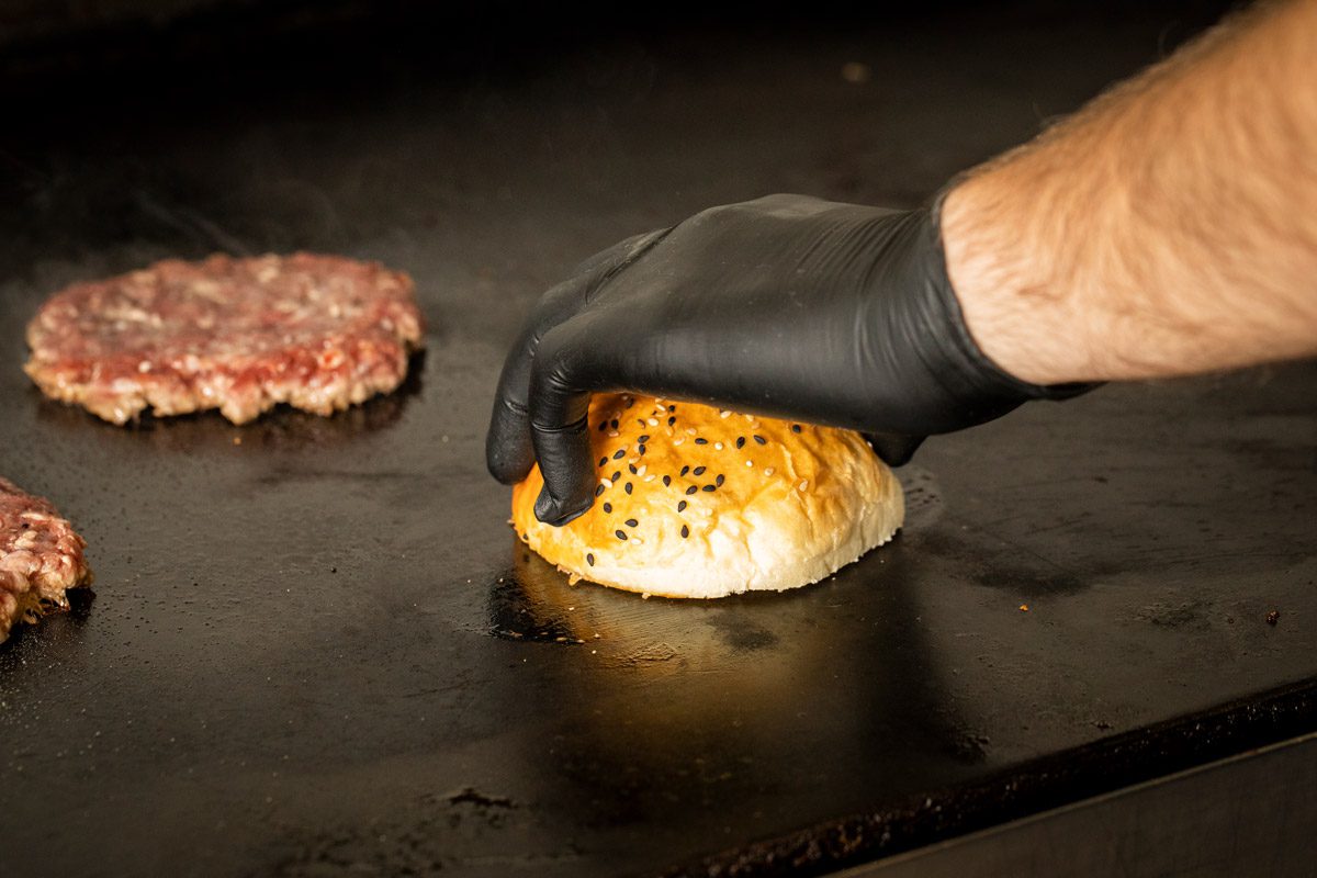 chef putting burger bun and meat on griddle