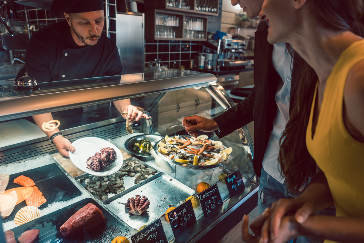 Chef choosing raw seafood from commercial display fridge